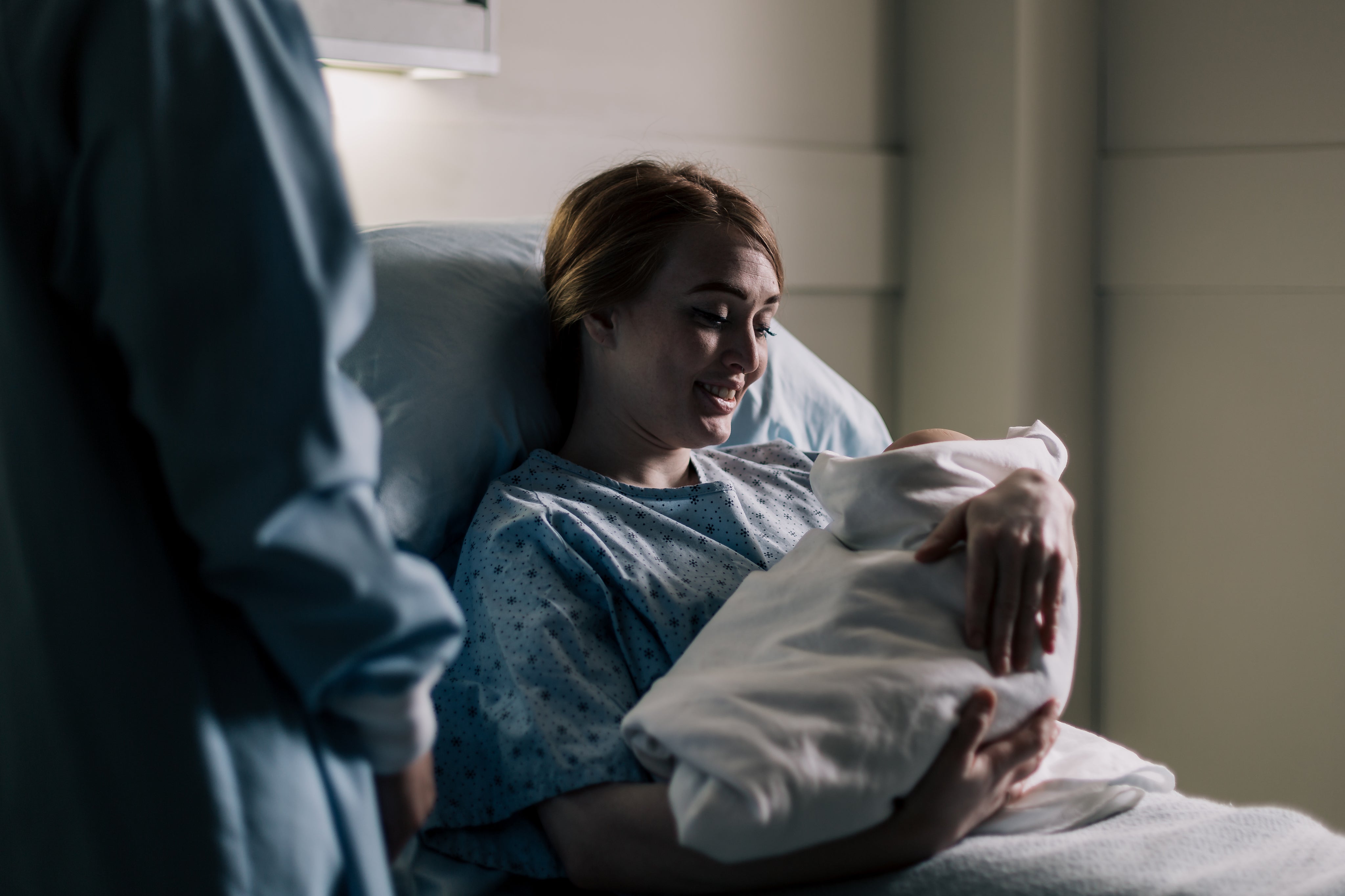 New mother resting in bed with her newborn baby in the first week postpartum