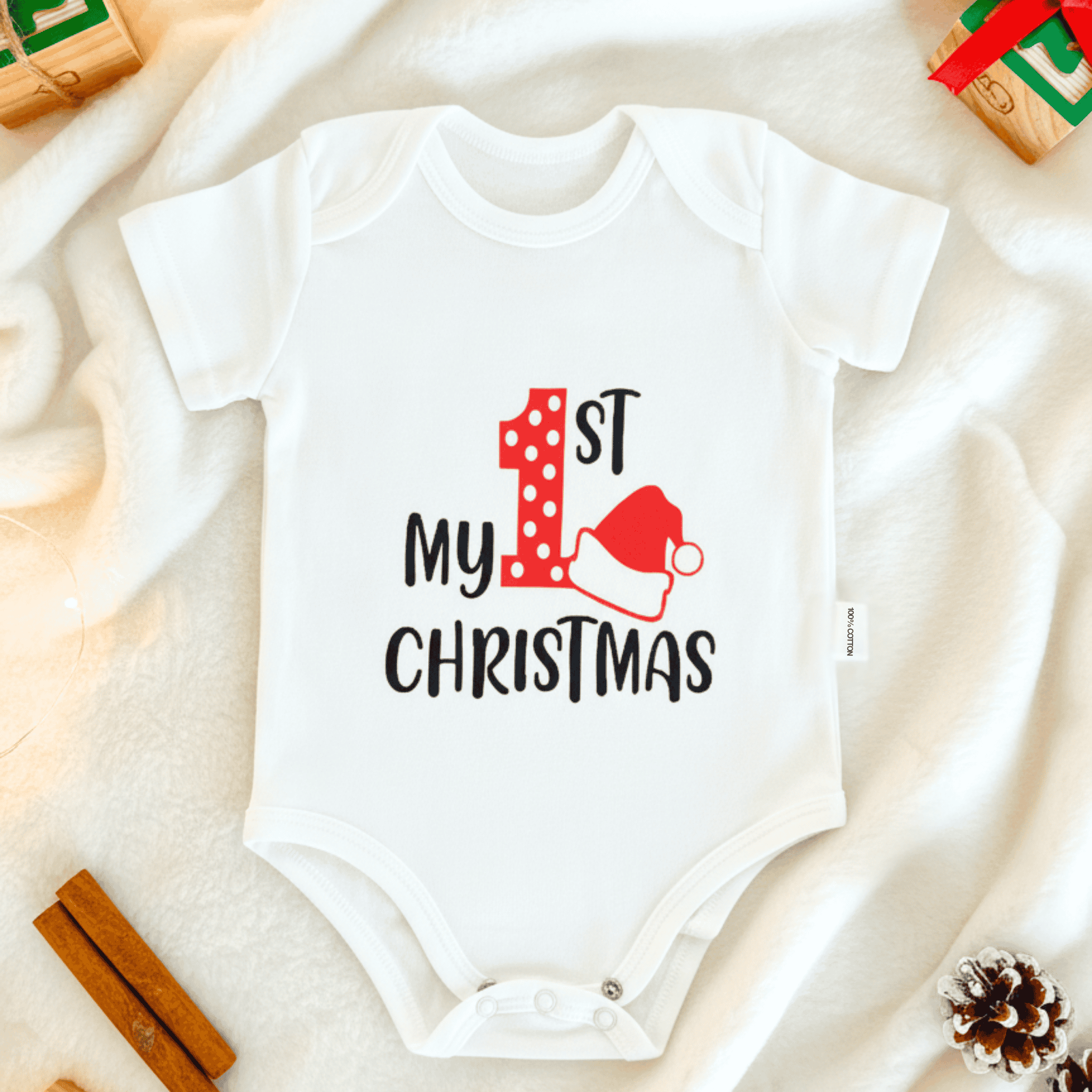 White baby onesie with 'First My Christmas' text on a soft surface.