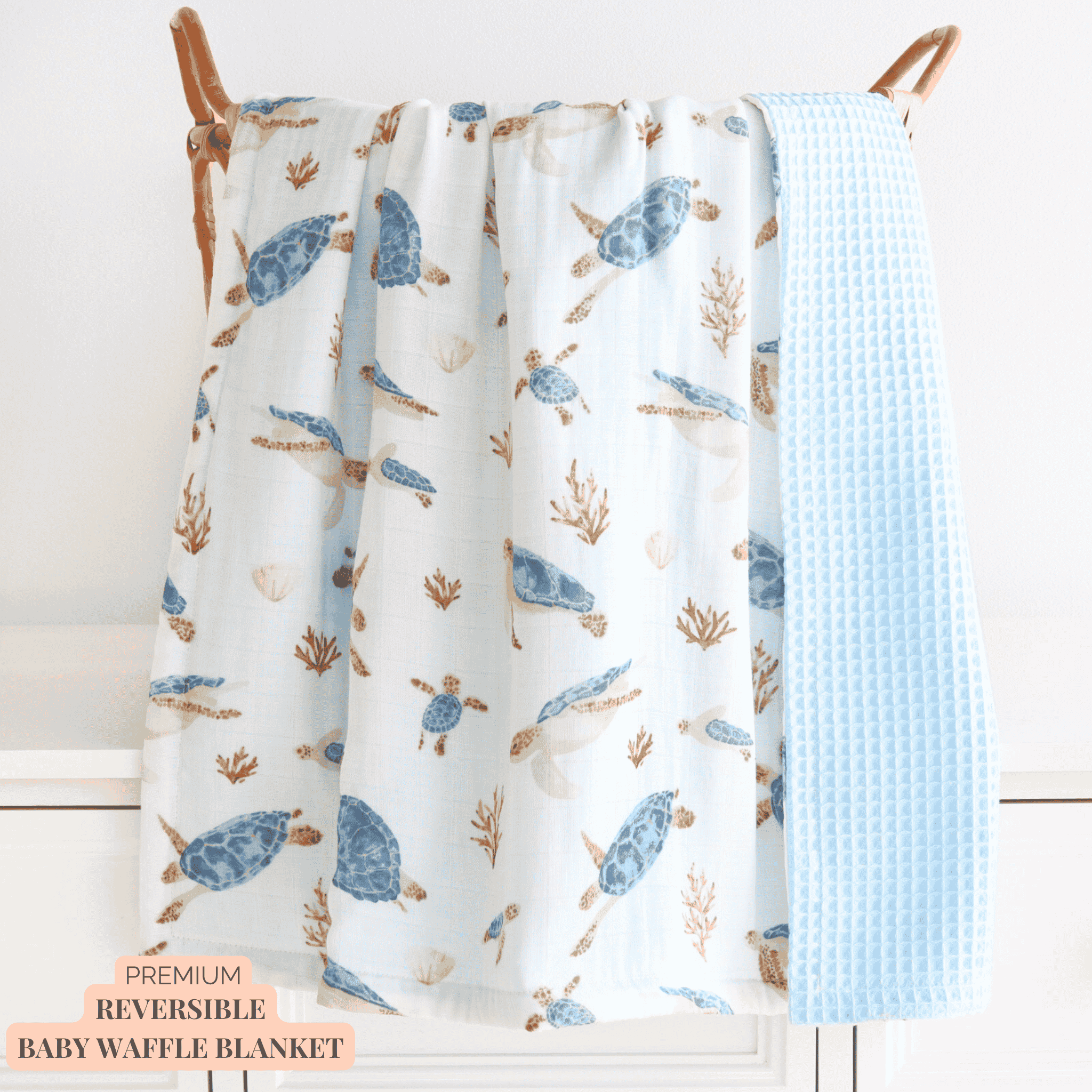 Reversible baby waffle blanket with turtle pattern on one side and solid blue on the other, hanging on wooden hangers.